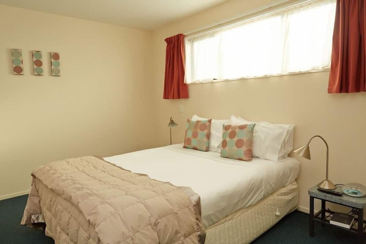 Um quarto com uma cama, uma mesa de cabeceira com abajur e uma janela com cortinas.