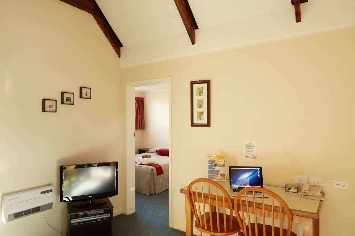 Quarto de hotel com televisão, escrivaninha com computador, uma cadeira e cama com cortina vermelha.