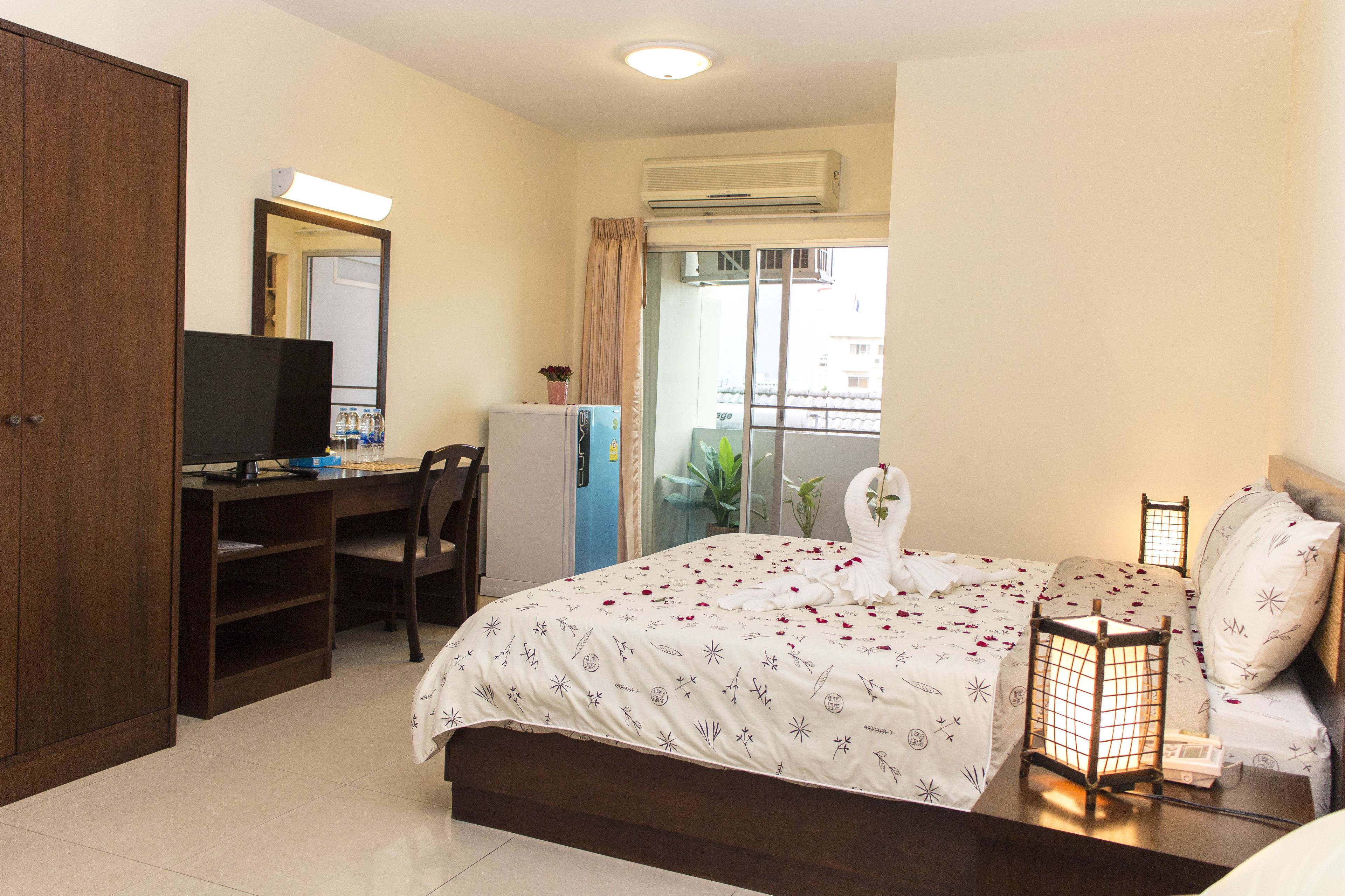 A bedroom with a bed, a desk, a chair, a wardrobe, and a balcony with plants.