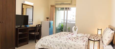 A bedroom with a bed, a desk, a chair, a wardrobe, and a balcony with plants.
