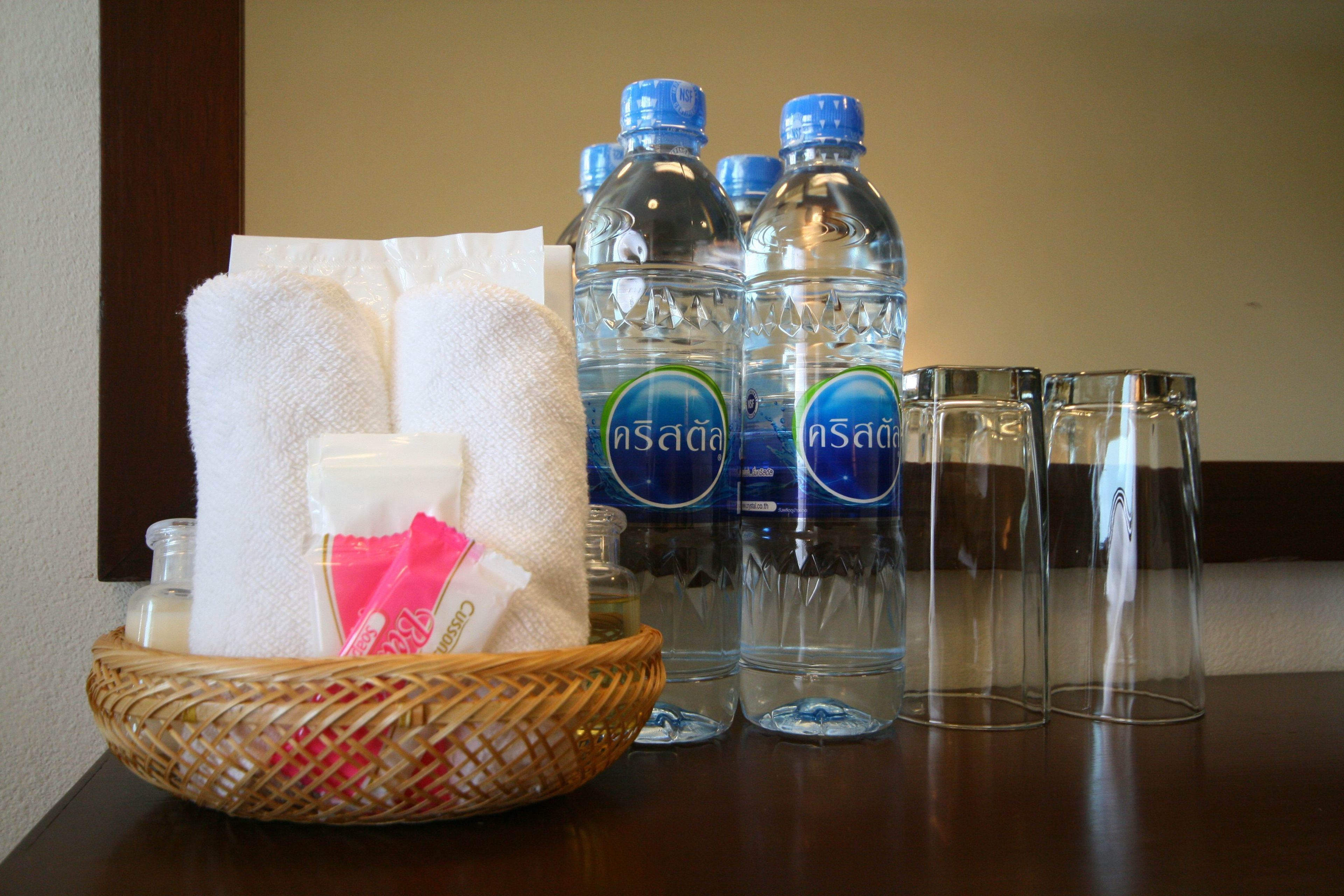 A table with a basket containing toiletries, a bottle of lotion, and a tissue. Behind the basket are several water bottles and glasses.