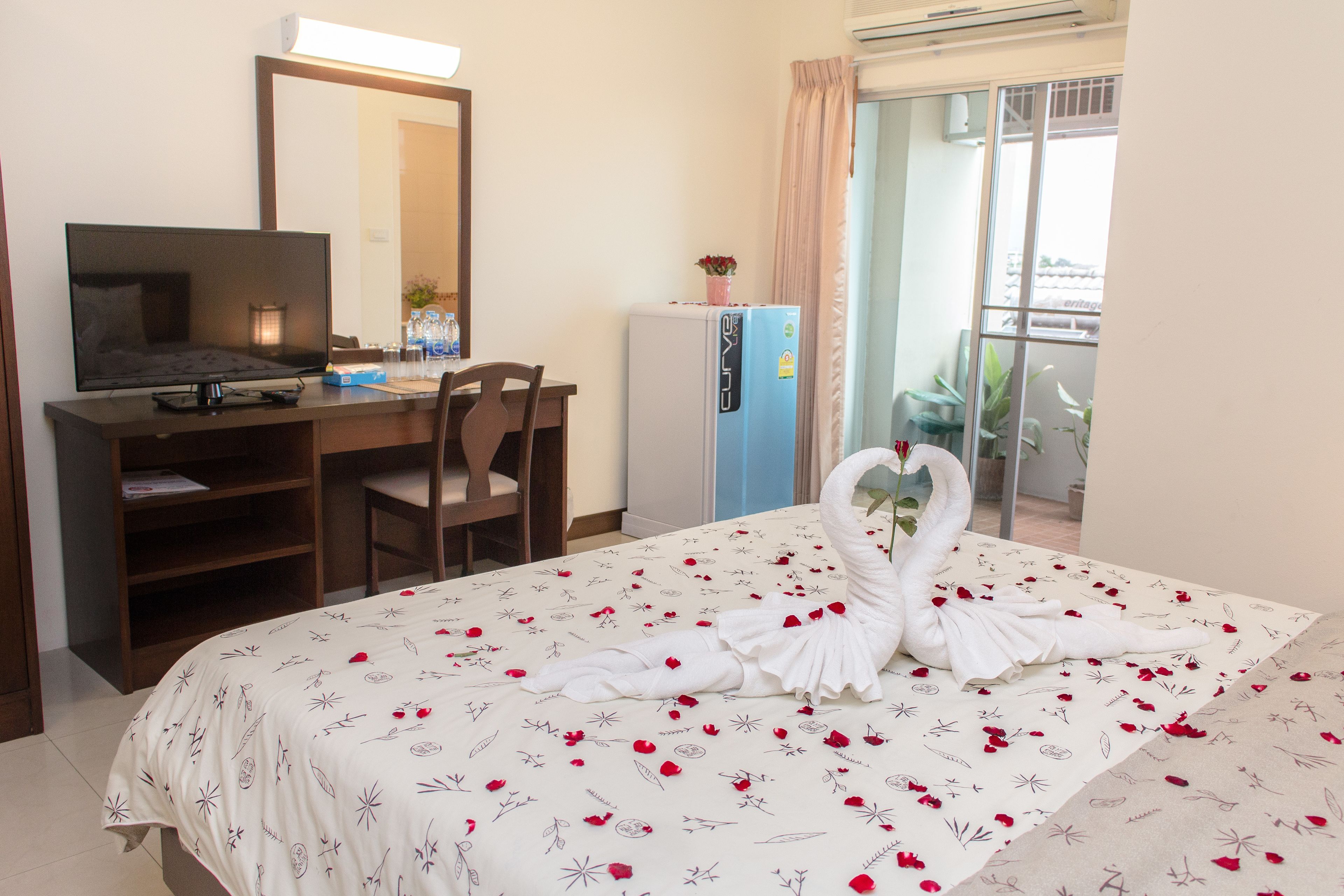 Una habitación de hotel con cama, escritorio con computadora, refrigerador y balcón con plantas.