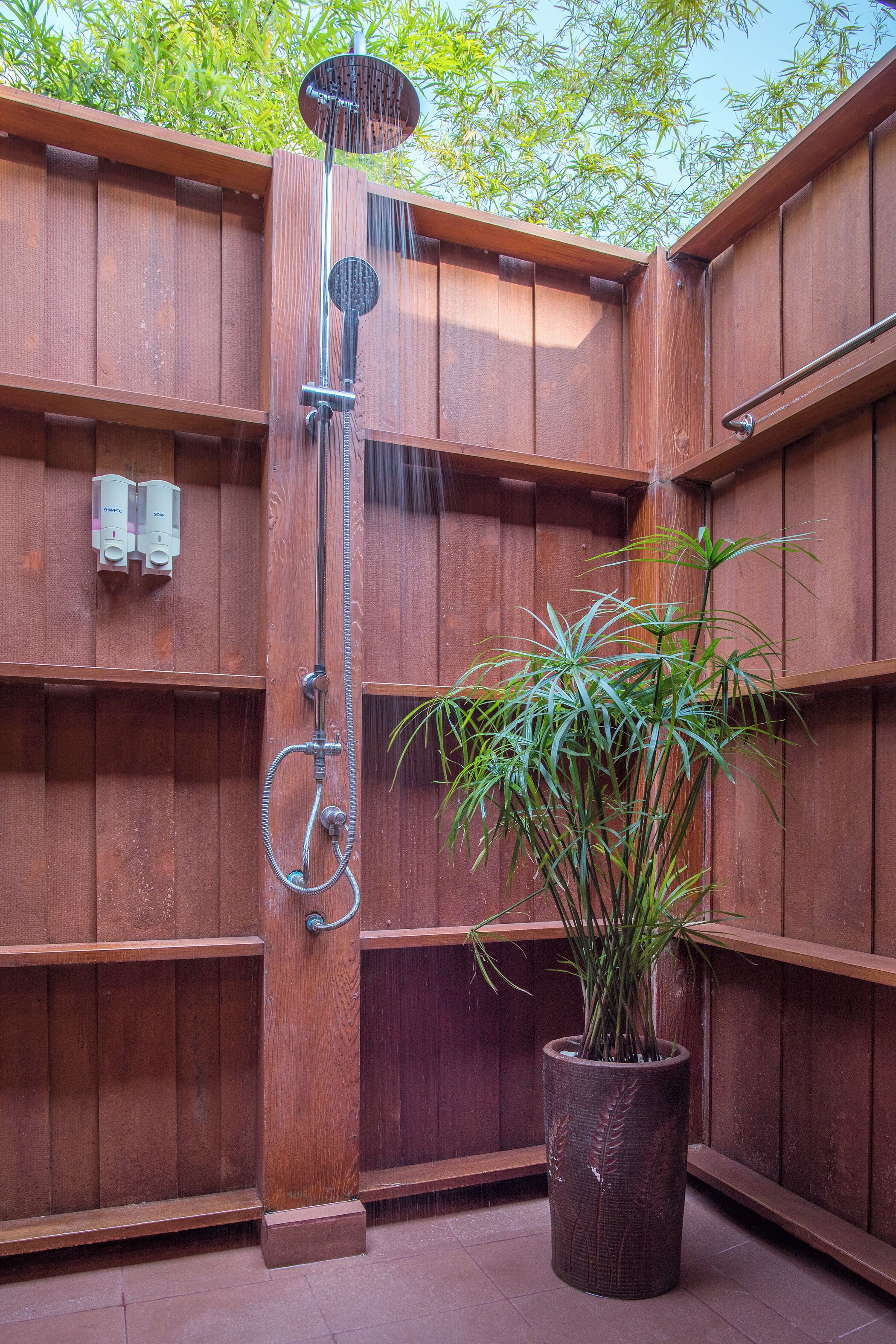 A wooden shower enclosure with a potted plant in the corner.