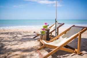 Una playa con dos sillas de madera y una pequeña mesa con una bebida y flores.