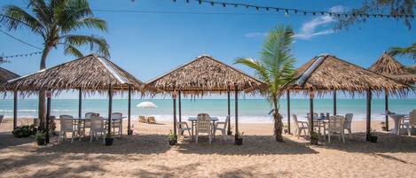 A beach with thatched umbrellas, white plastic chairs, and potted plants.