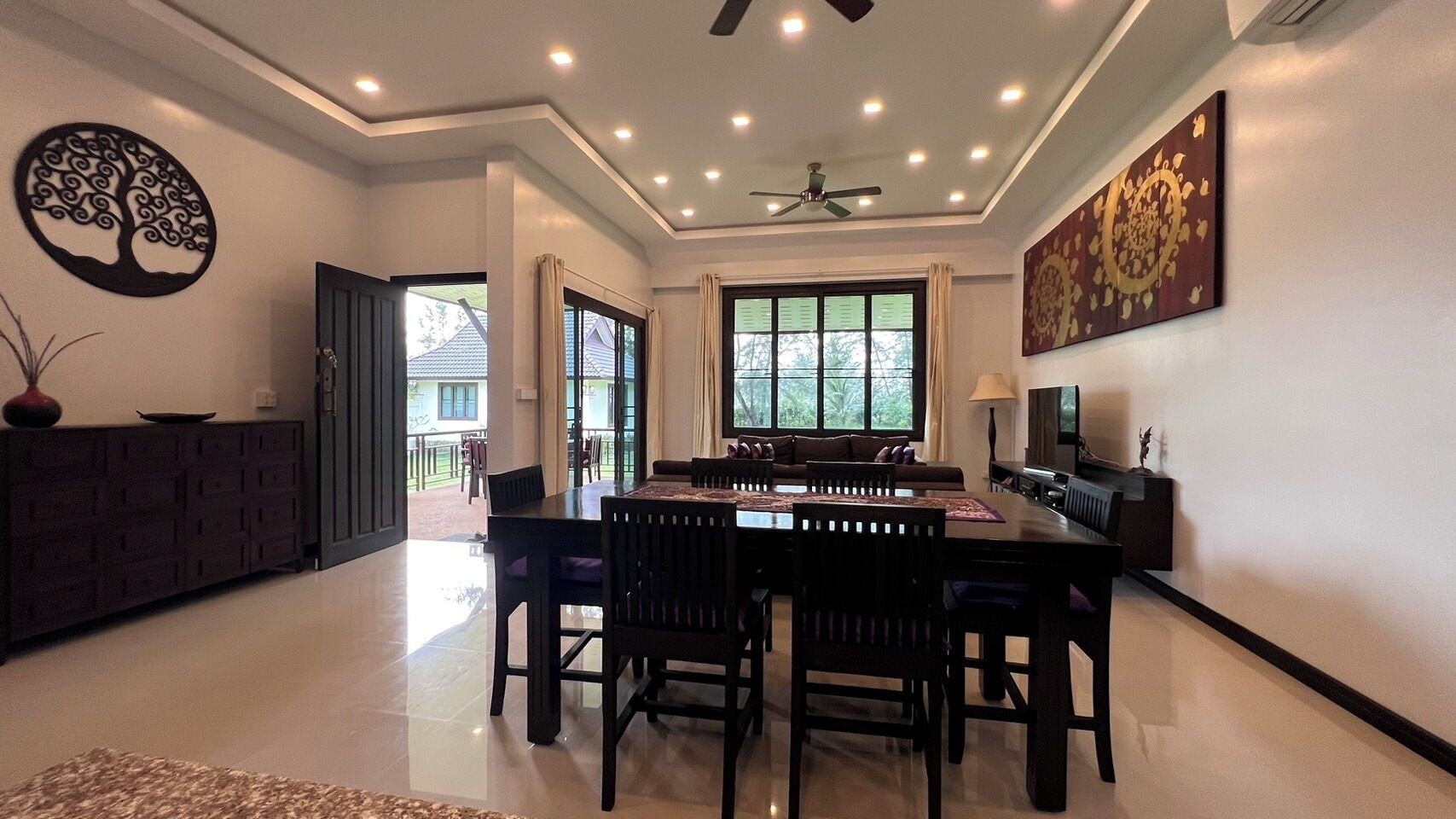 A spacious dining area with a high ceiling, a ceiling fan, and a large window providing natural light.