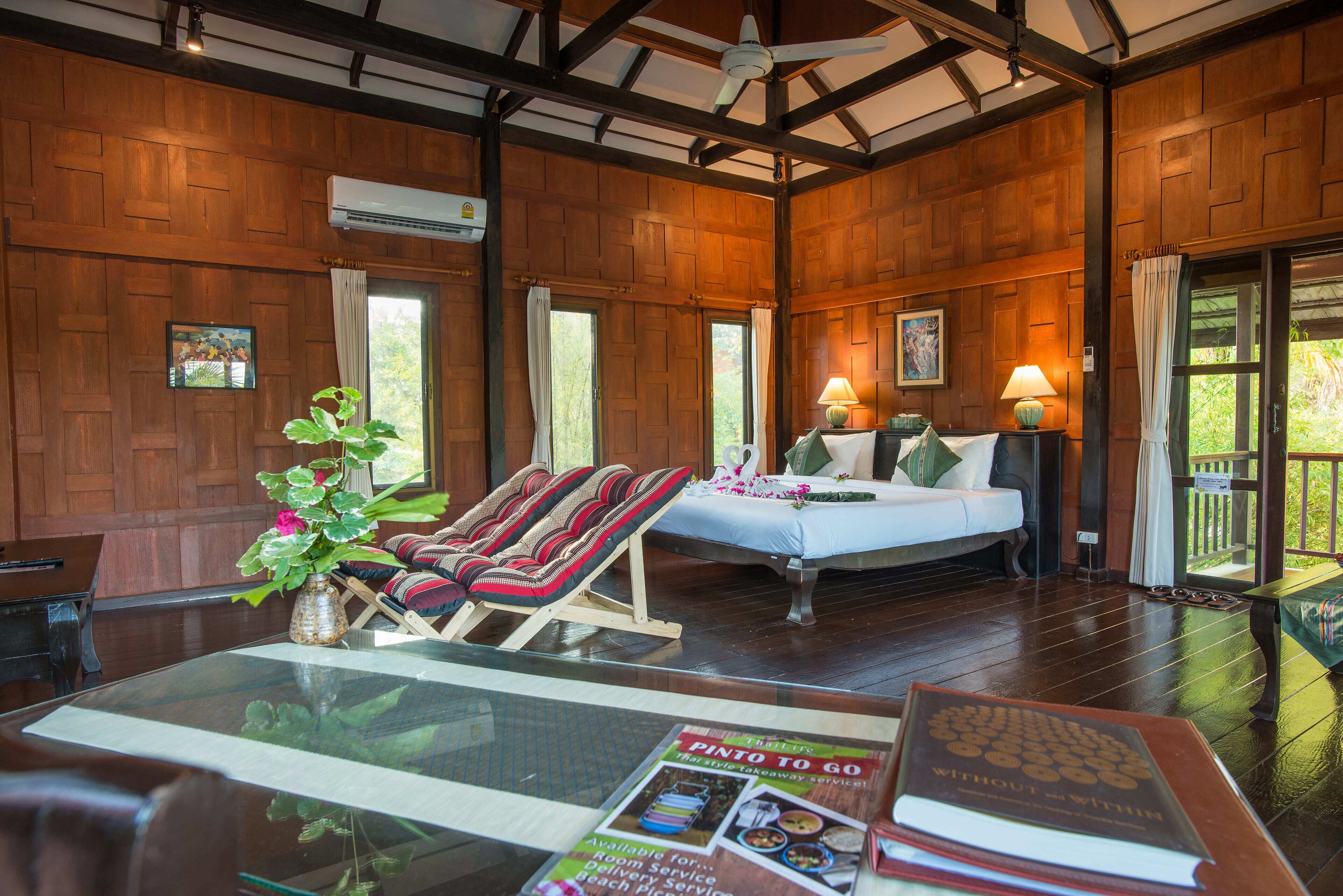 A wooden room with a bed, a lounge chair, and a table with a magazine.