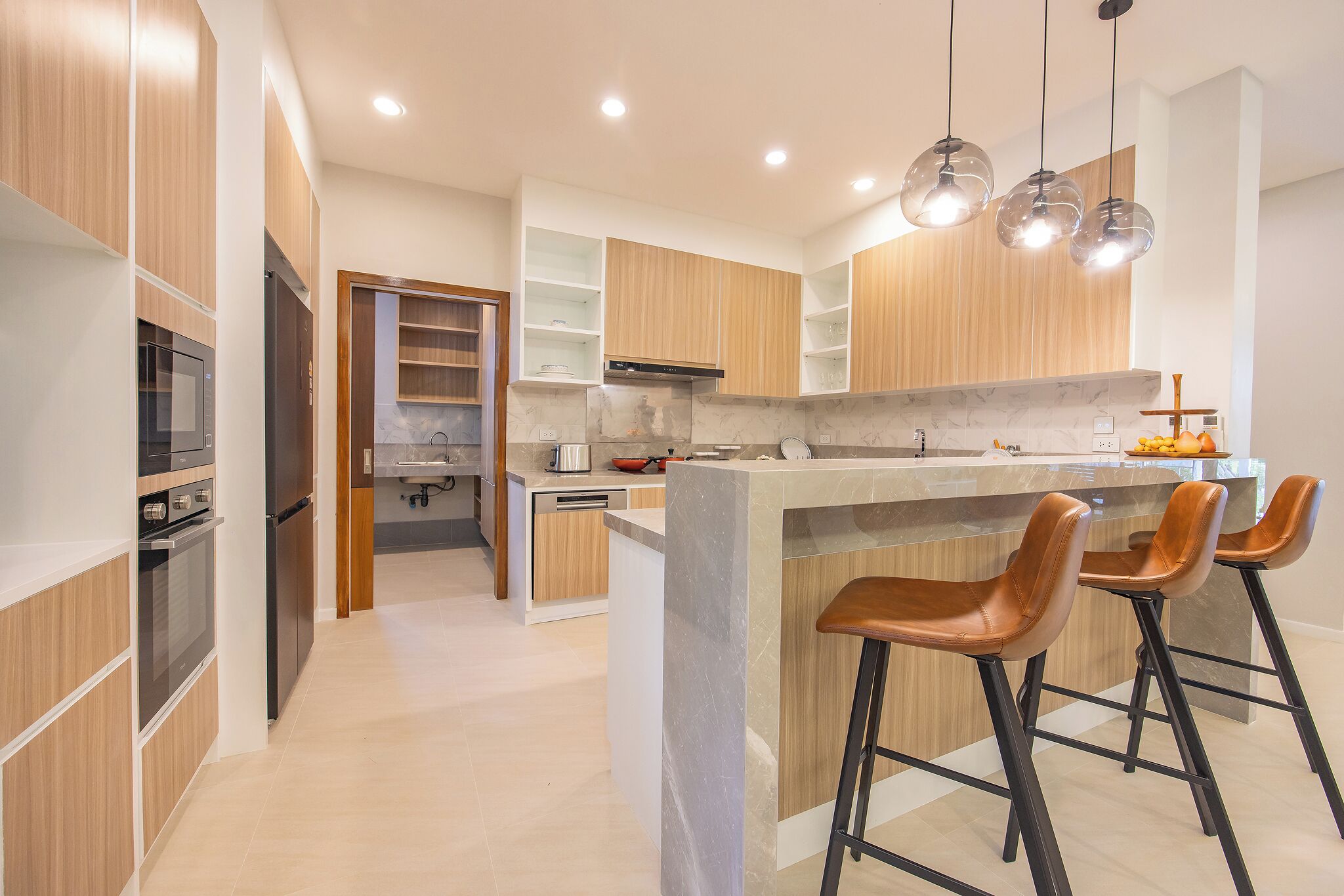 A modern kitchen with wooden cabinets, a central island with stools, and pendant lighting.