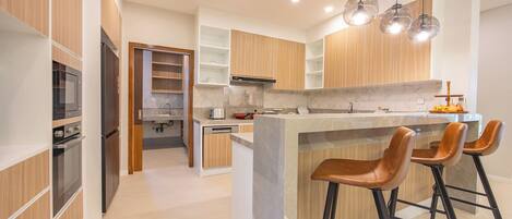 A modern kitchen with wooden cabinets, a central island with stools, and pendant lighting.