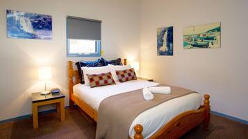 A neatly arranged bedroom with a bed, bedside table, lamp, and two wall-mounted paintings.