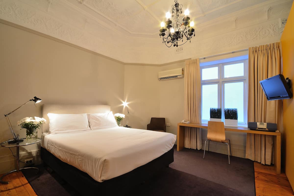 Une chambre d’hôtel avec un lit, un bureau, une chaise, une télévision et un lustre.