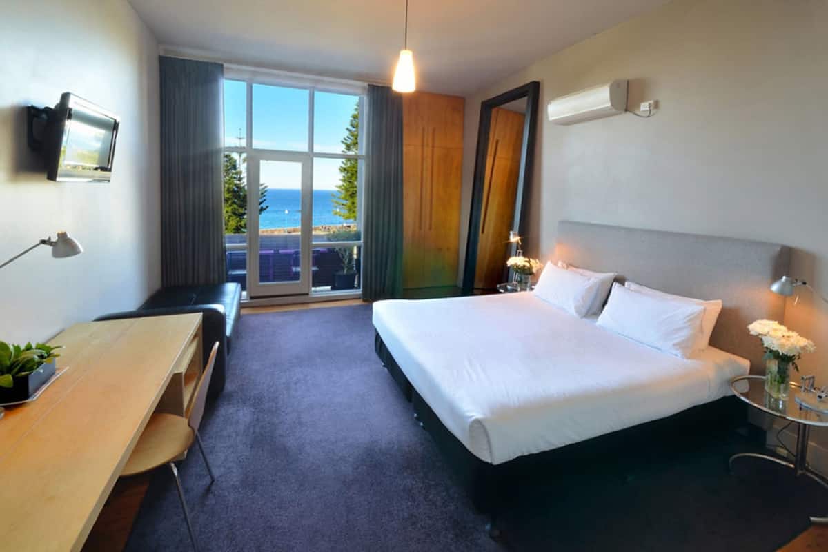 Une chambre d’hôtel avec un lit, un bureau, une chaise, une télévision et une vue sur la mer.