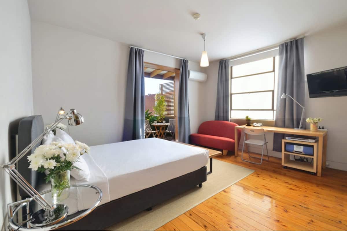 Une chambre d’hôtel moderne équipée d’un lit, d’un bureau, d’une chaise et d’un téléviseur fixé au mur.