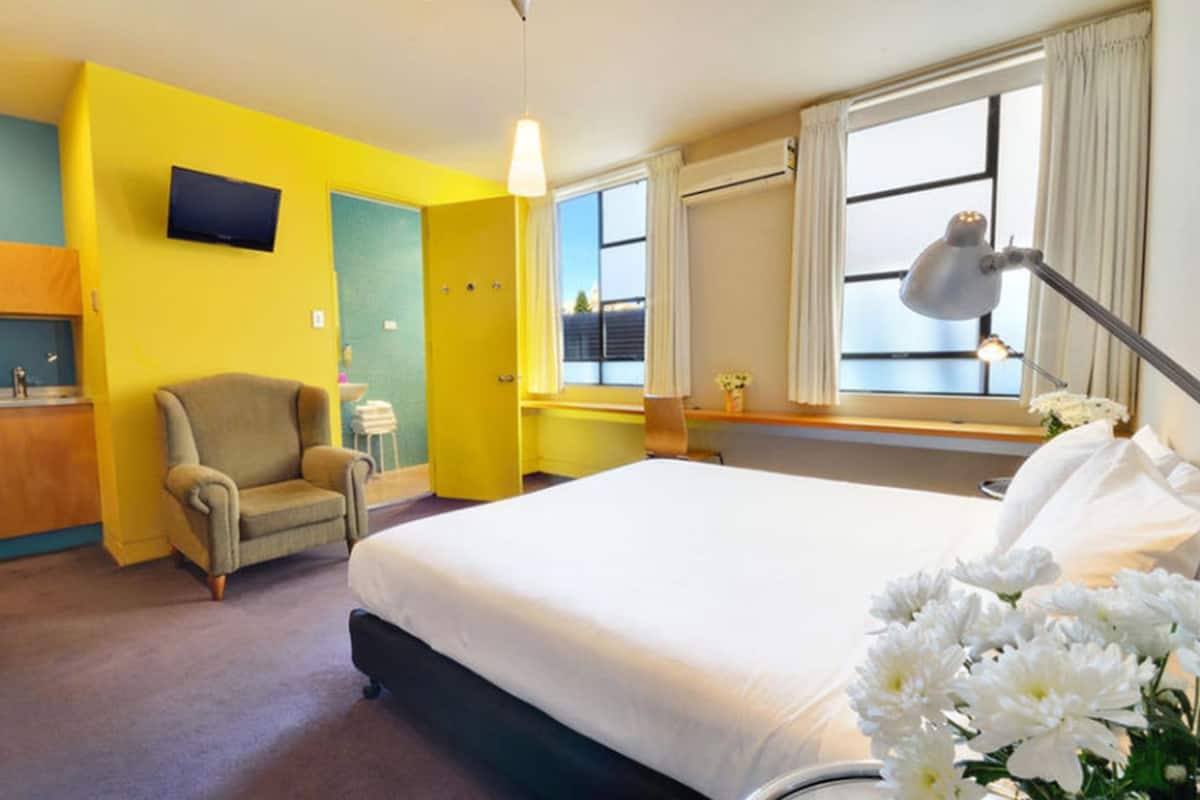 Une chambre d’hôtel avec un lit, une chaise, un bureau, une télévision et une fenêtre avec des rideaux.