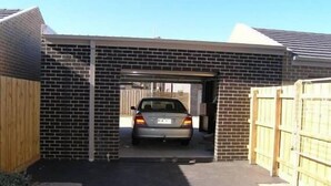 A garage with a car parked inside, a wooden fence on one side, and a brick wall on the other. - Insaa Serviced Apartments Dandenong (Dandenong)