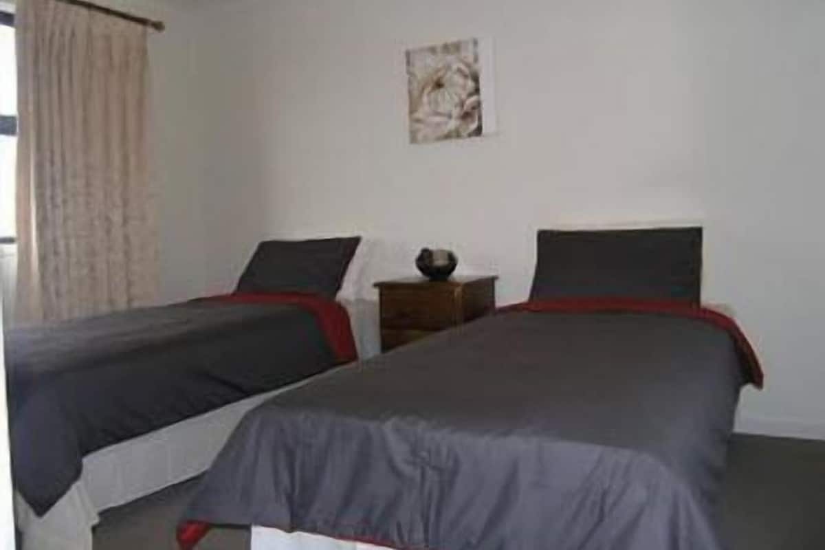 Een kamer met twee bedden, een tafeltje en een schilderij aan de muur.
