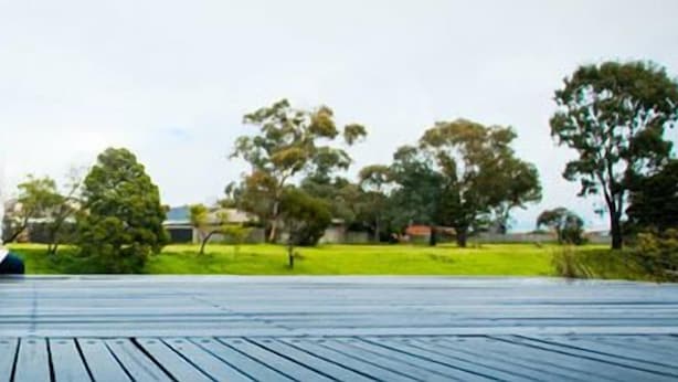 A person sitting on a wooden deck with a view of a green park and houses in the background. - Insaa Serviced Apartments Dandenong (Dandenong)
