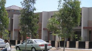 A modern building with a flat roof and brick facade, surrounded by green trees and a parked car. - Insaa Serviced Apartments Dandenong (Dandenong)