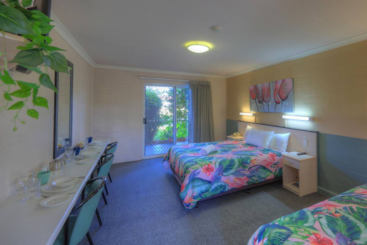 A hotel room with two beds, a desk, a chair, a mirror, and a bathroom area.