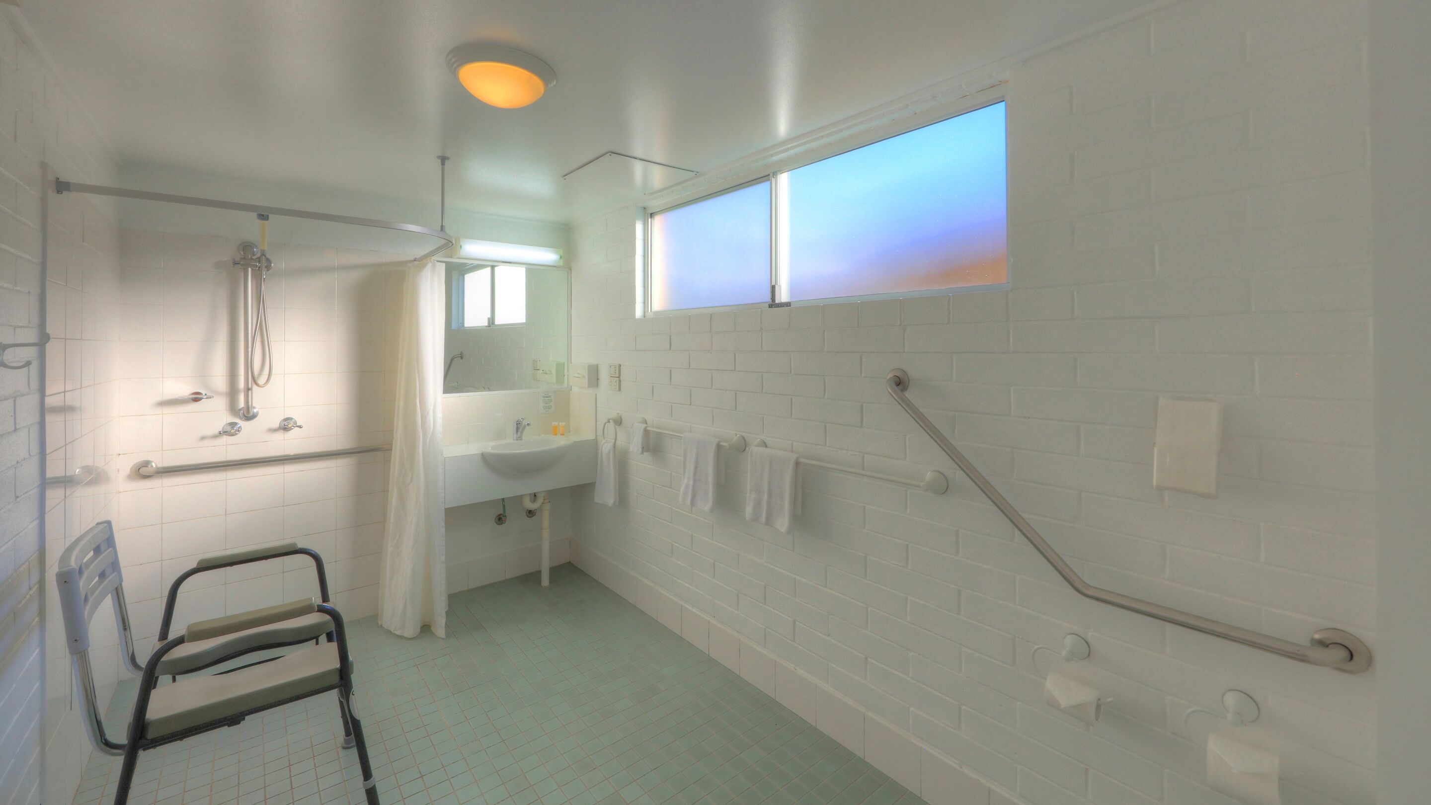 A bathroom with a shower, a sink, a mirror, and a window.