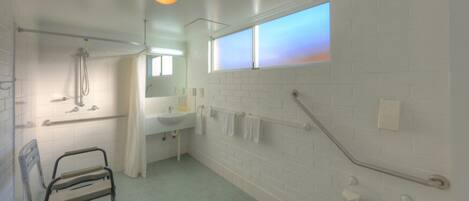 A bathroom with a shower, a sink, a mirror, and a window.