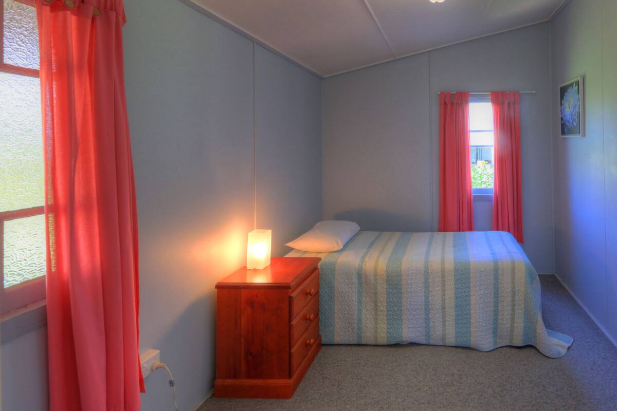 A bedroom with a bed, a nightstand, a window with curtains, and a wall-mounted picture.
