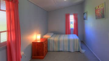 Un dormitorio con cama, mesita de noche, ventana con cortinas e imagen colgada en la pared.