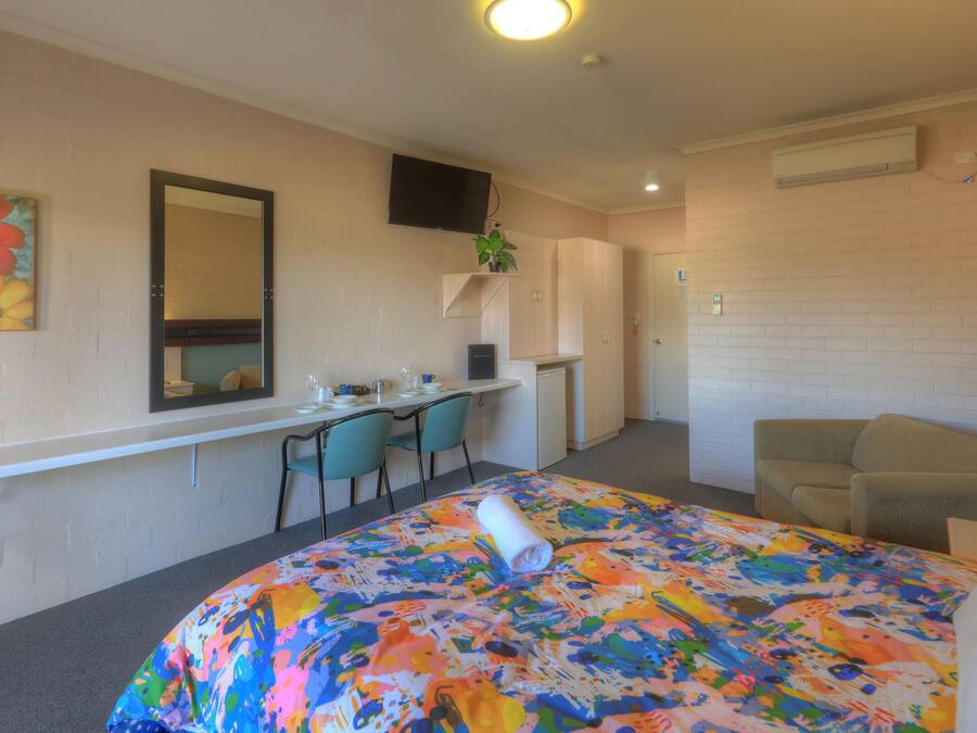 A hotel room with a bed, a desk, a chair, a TV, and a mirror.