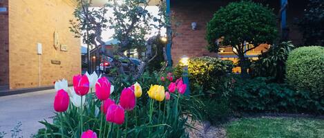 Un jardín con tulipanes frente a un edificio de fachada de ladrillo y balcón azul.