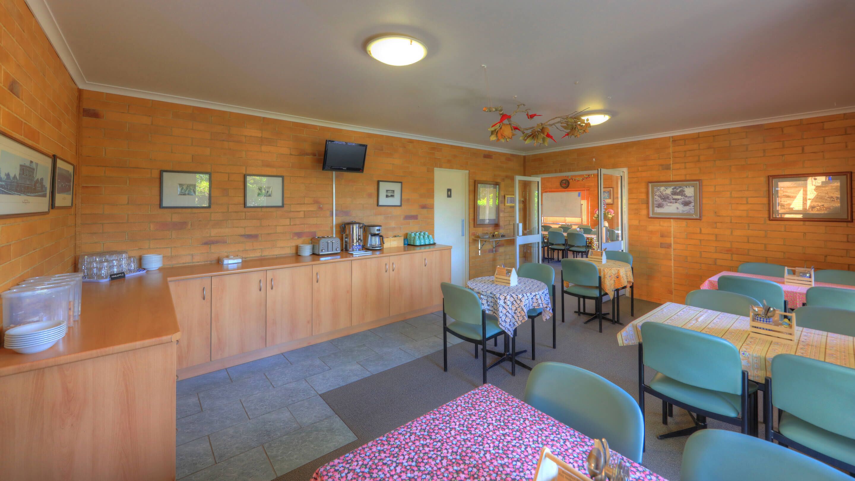 A dining area with wooden cabinets, a television, and framed pictures on the walls.