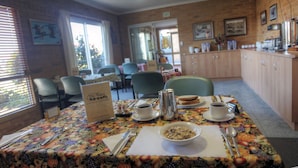 A dining area with a table set for breakfast, including a bowl of cereal, coffee cups, and a menu sign. - The Vines Motel and Cottages (Stanthorpe)