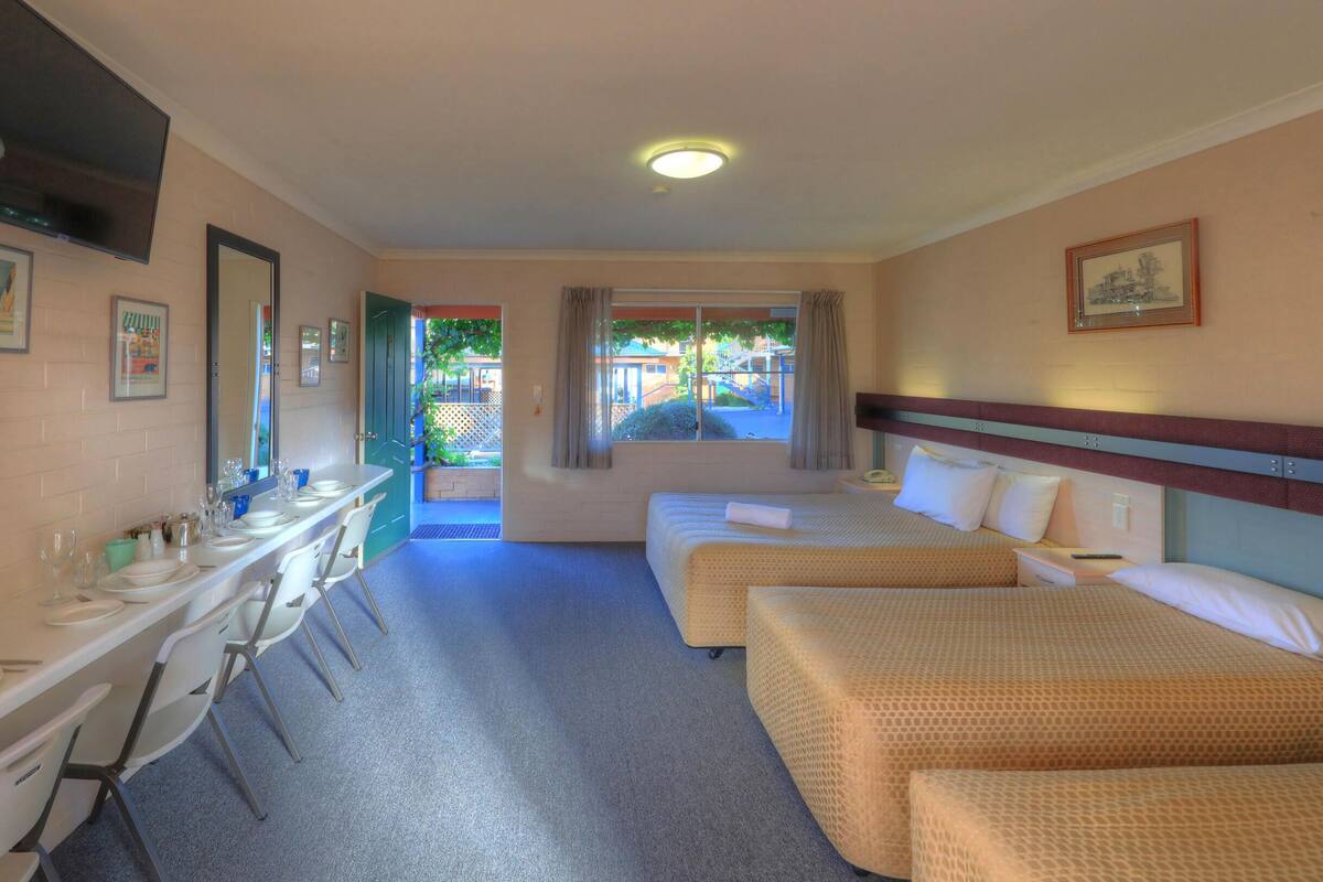 A hotel room with a dining area, two single beds, a desk, and a TV.