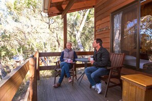 Una terraza de madera con dos personas sentadas en una mesa, rodeadas de árboles.