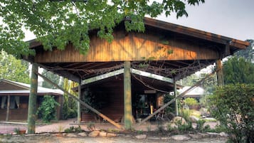 A rustic wooden structure with a metal frame, surrounded by a garden with rocks and plants.