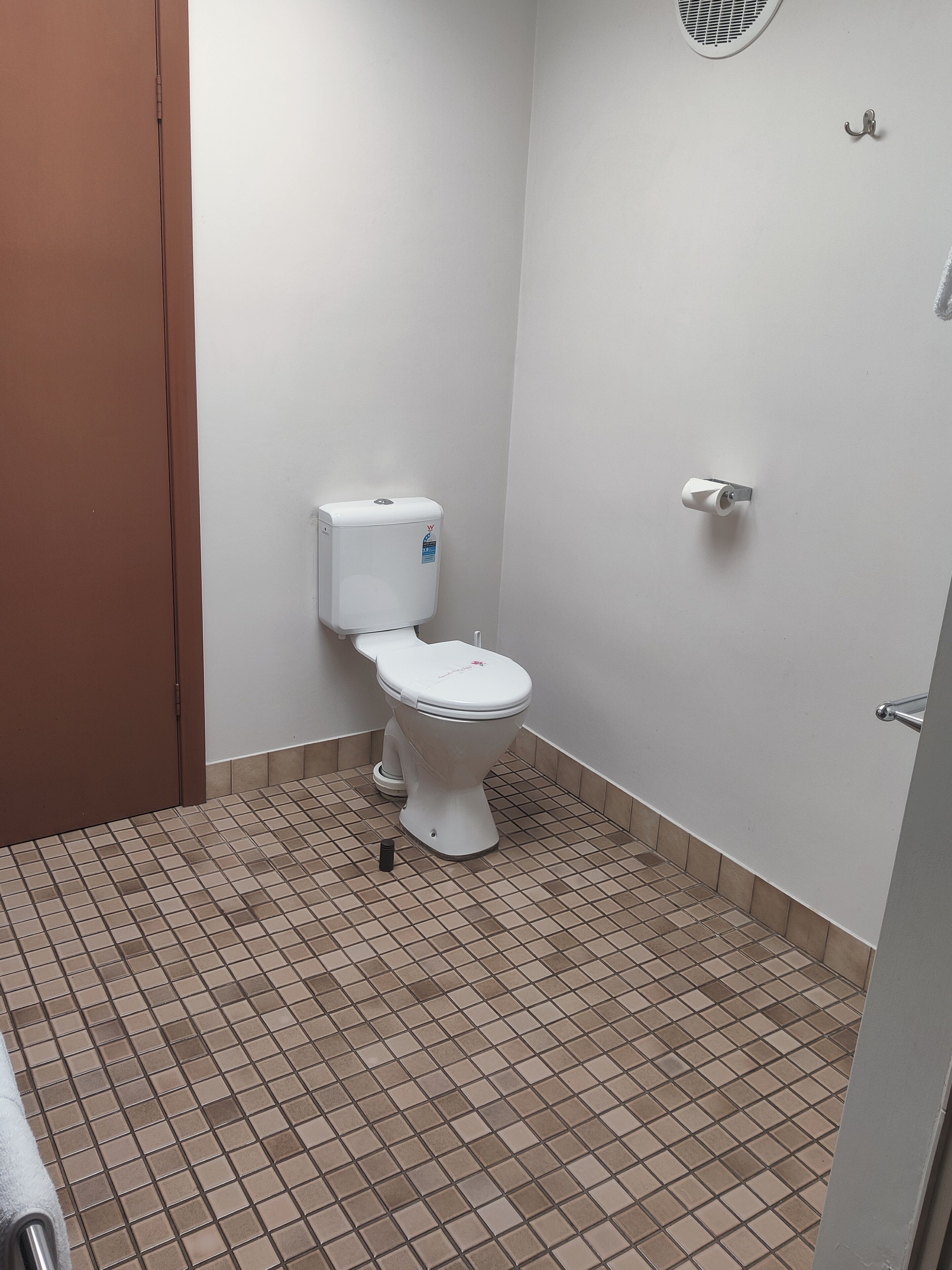 Un baño pequeño y limpio con inodoro, secador de manos y barra para toallas.