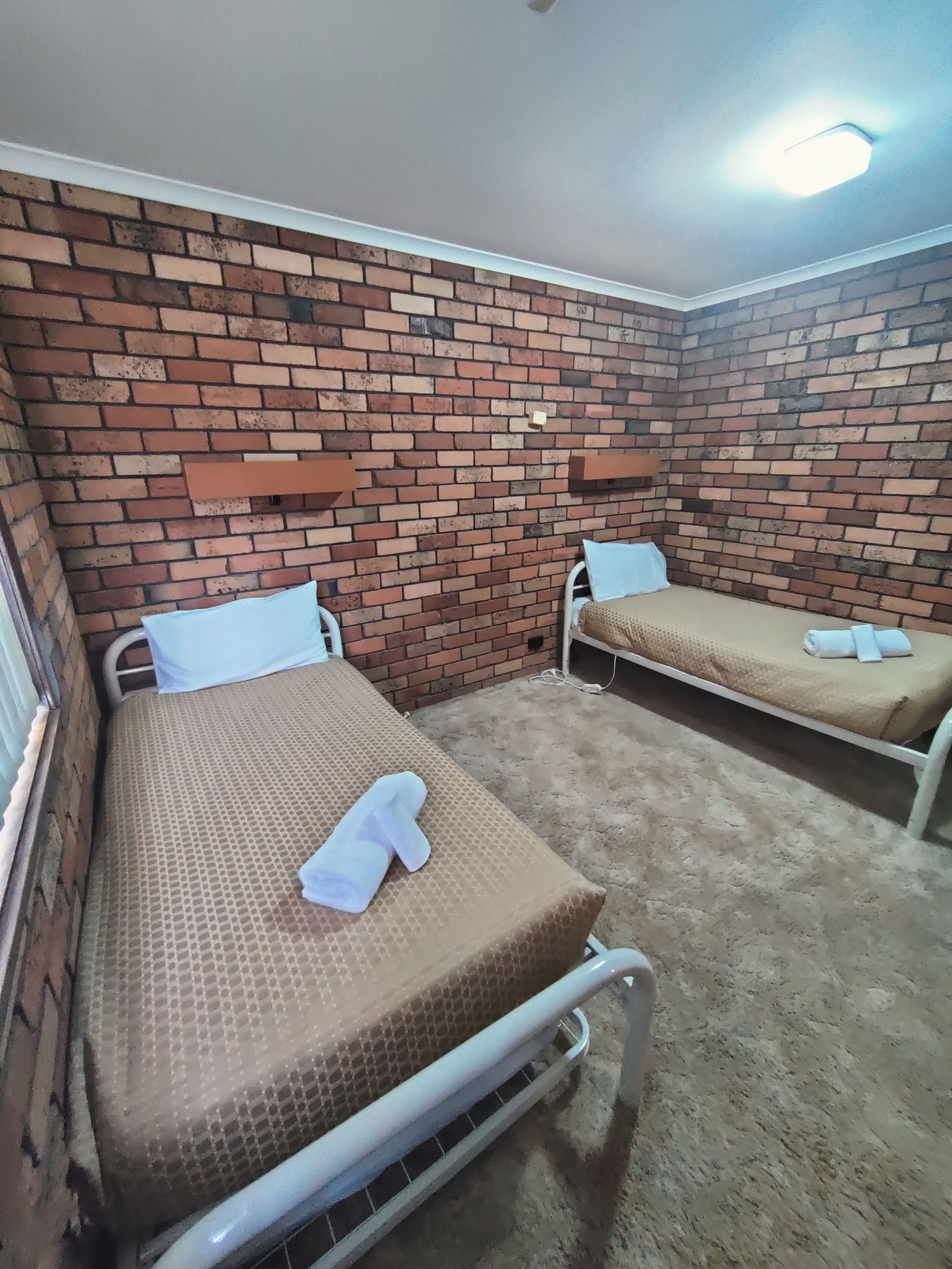 Habitación con dos camas, pared de ladrillo y una lámpara en el techo.
