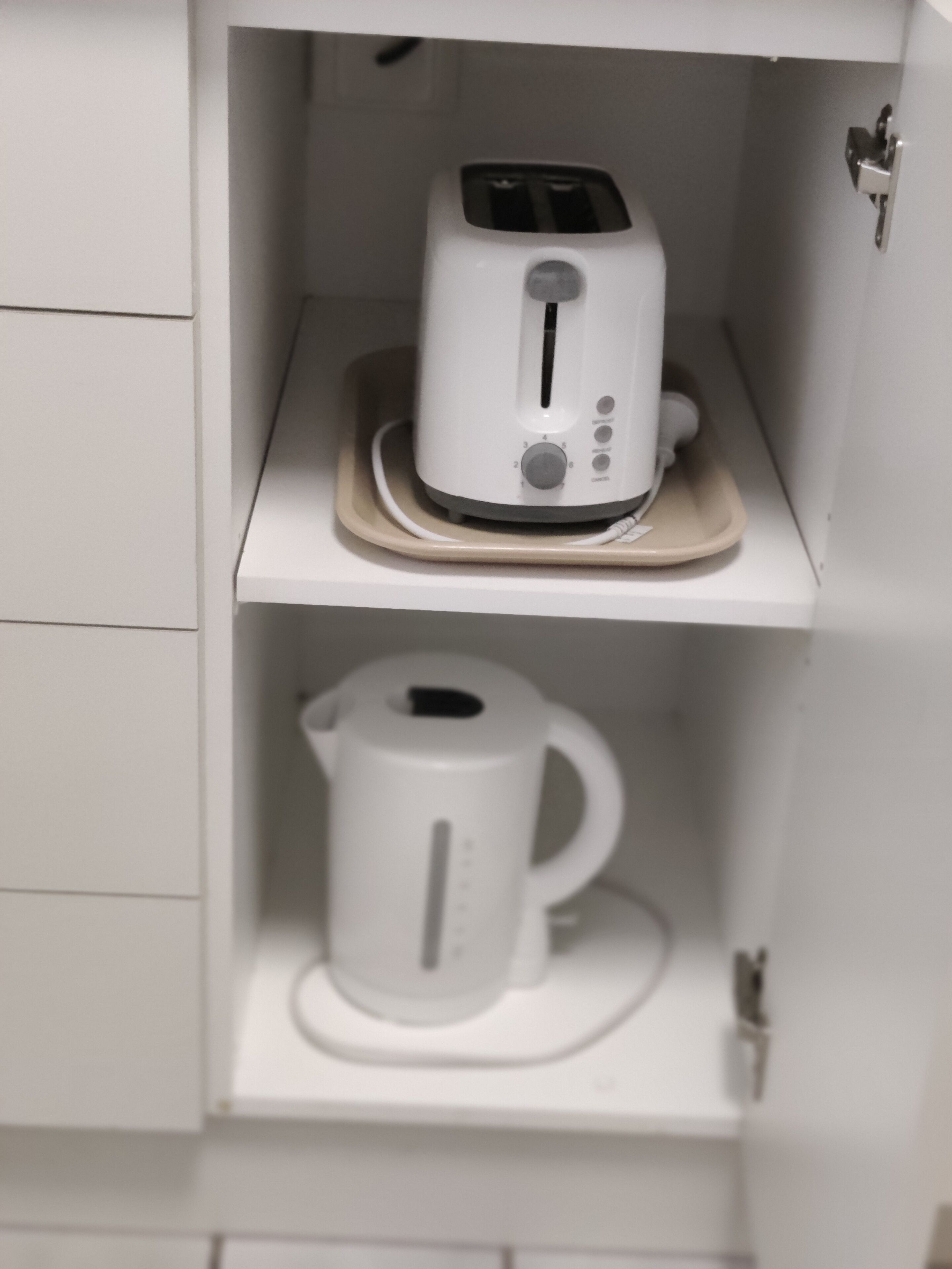 Un mueble de cocina blanco con un tostador y una tetera eléctrica blanca en estantes separados.