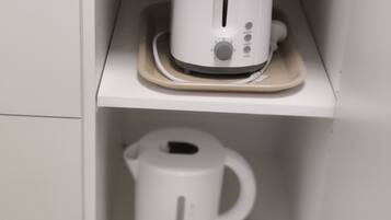 Un mueble de cocina blanco con un tostador y una tetera eléctrica blanca en estantes separados.
