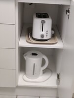 Un mueble de cocina blanco con un tostador y una tetera eléctrica blanca en estantes separados.