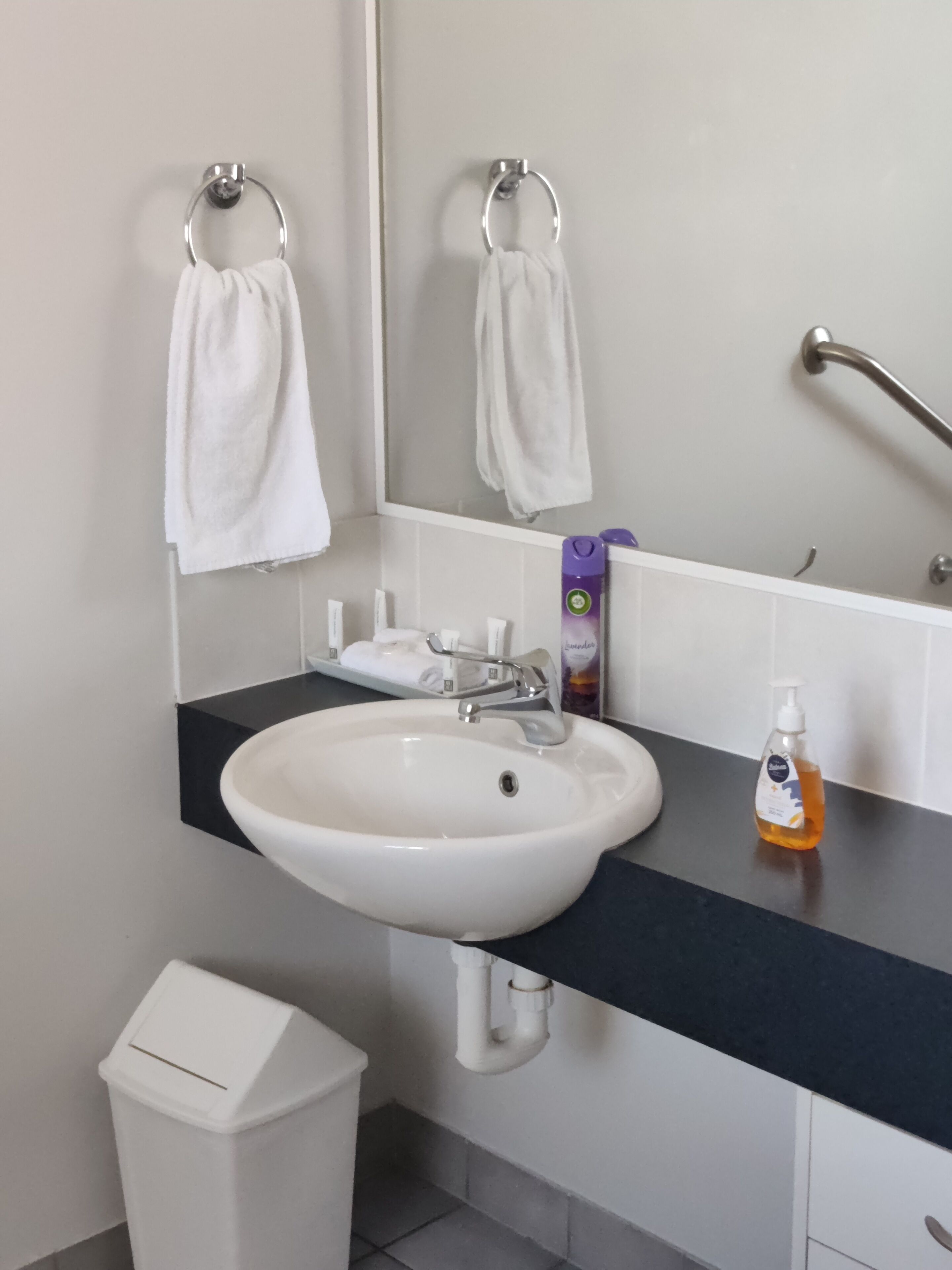 A bathroom with a white sink, a mirror, a hand dryer, and a trash bin.