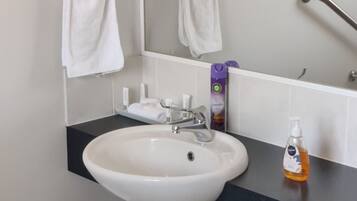 A bathroom with a white sink, a mirror, a hand dryer, and a trash bin.