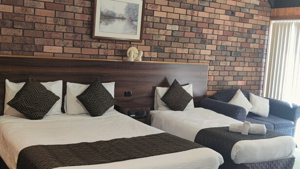 Een hotelkamer met twee bedden, een bakstenen muur, een lijst met een foto en een houten plafond.