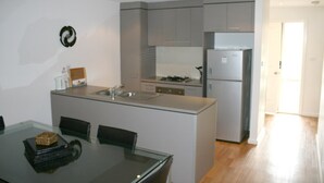 A modern kitchen with grey cabinets, a built-in island with a sink, and a refrigerator. - Grand Manor Motor Inn - Queanbeyan (Queanbeyan East)