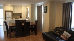 A modern living room with a black leather sofa and a dining area with a wooden table and chairs. - Grand Manor Motor Inn - Queanbeyan (Queanbeyan East)