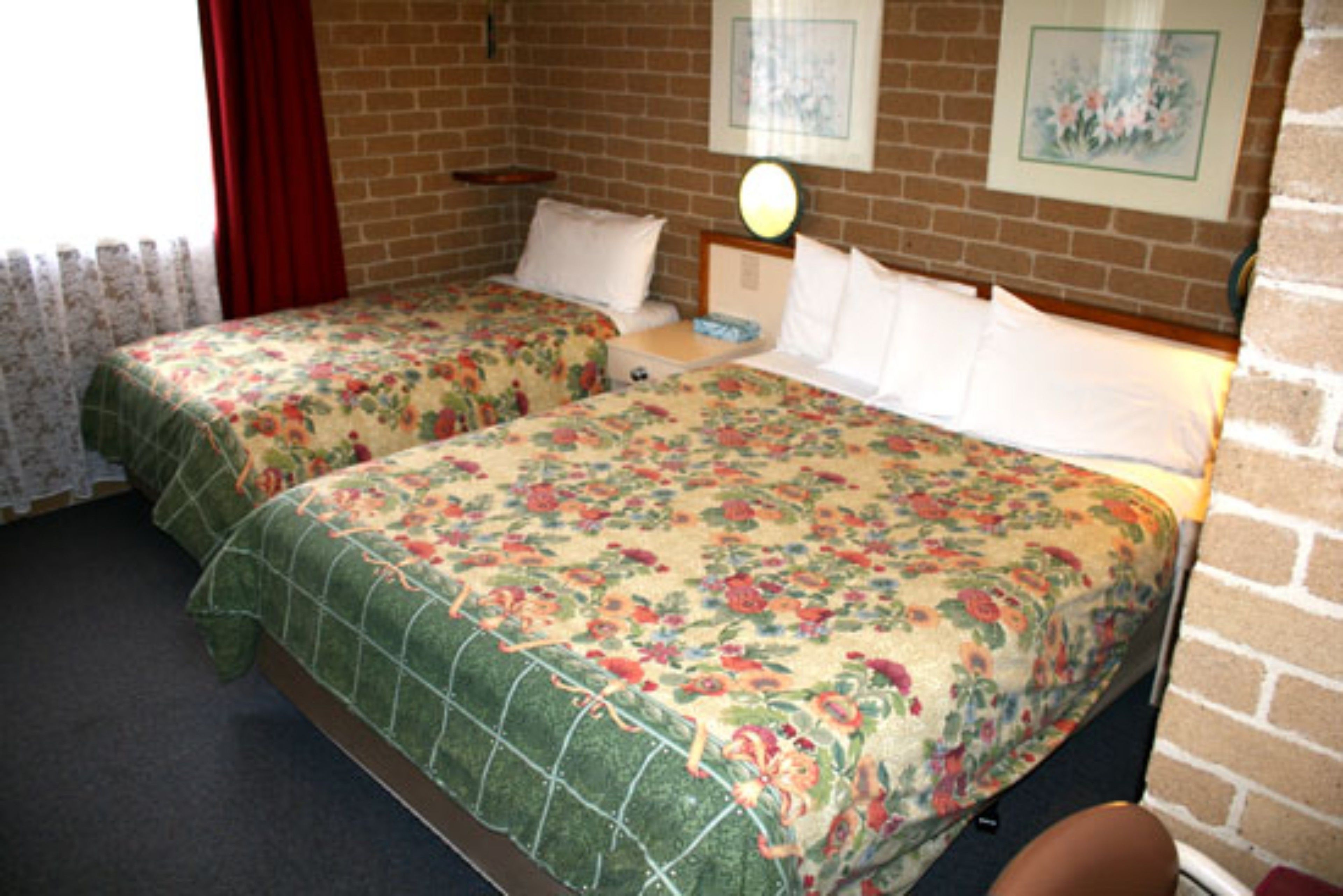 Una habitación con dos camas, una pared de ladrillo y una ventana con cortinas rojas.
