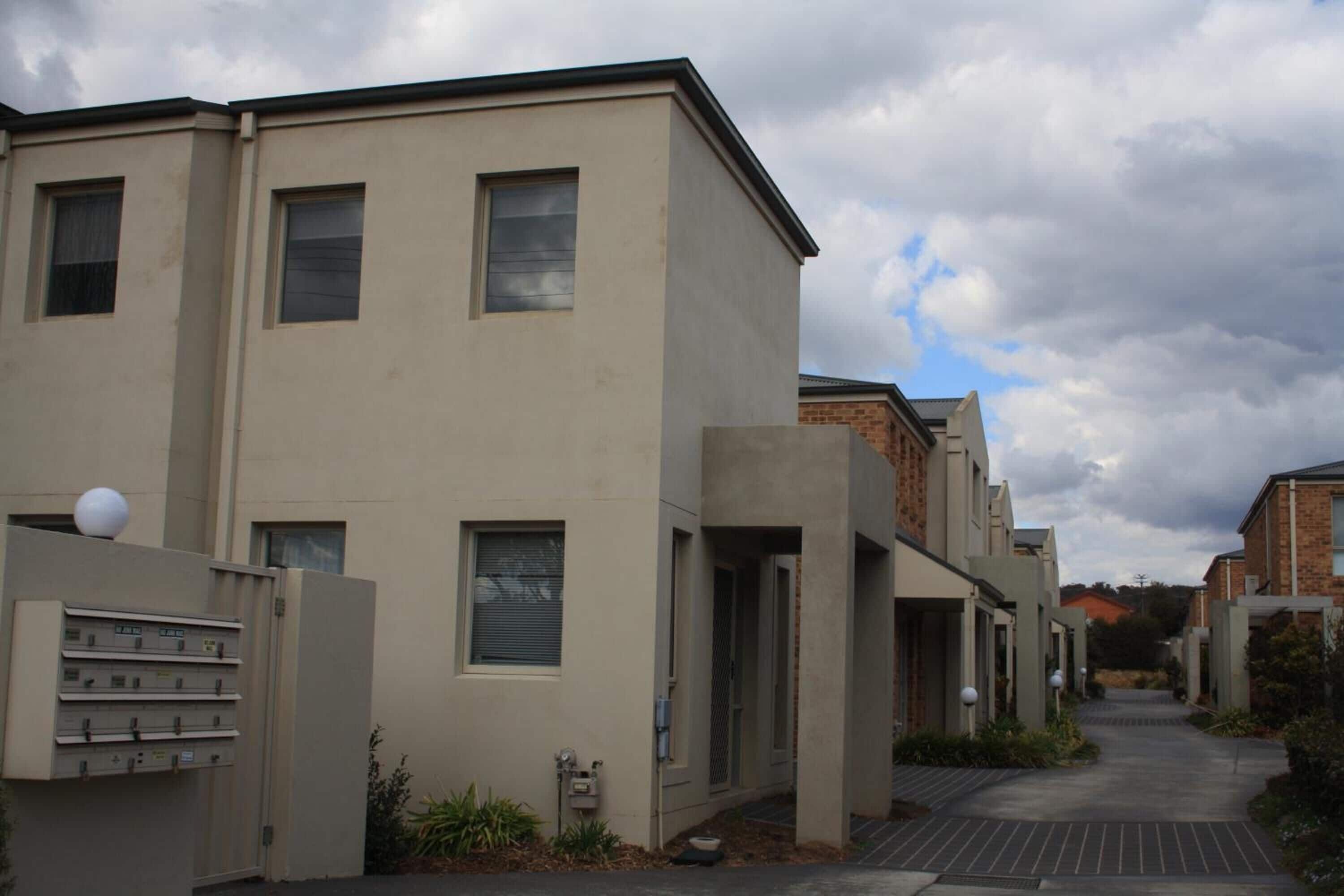 A modern residential building with a flat facade, multiple windows, and a gated entrance.