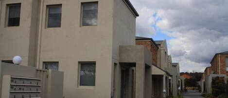 A modern residential building with a flat facade, multiple windows, and a gated entrance.