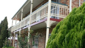 A two-story building with a balcony on the second floor, surrounded by greenery and a brick facade. - Grand Manor Motor Inn - Queanbeyan (Queanbeyan East)