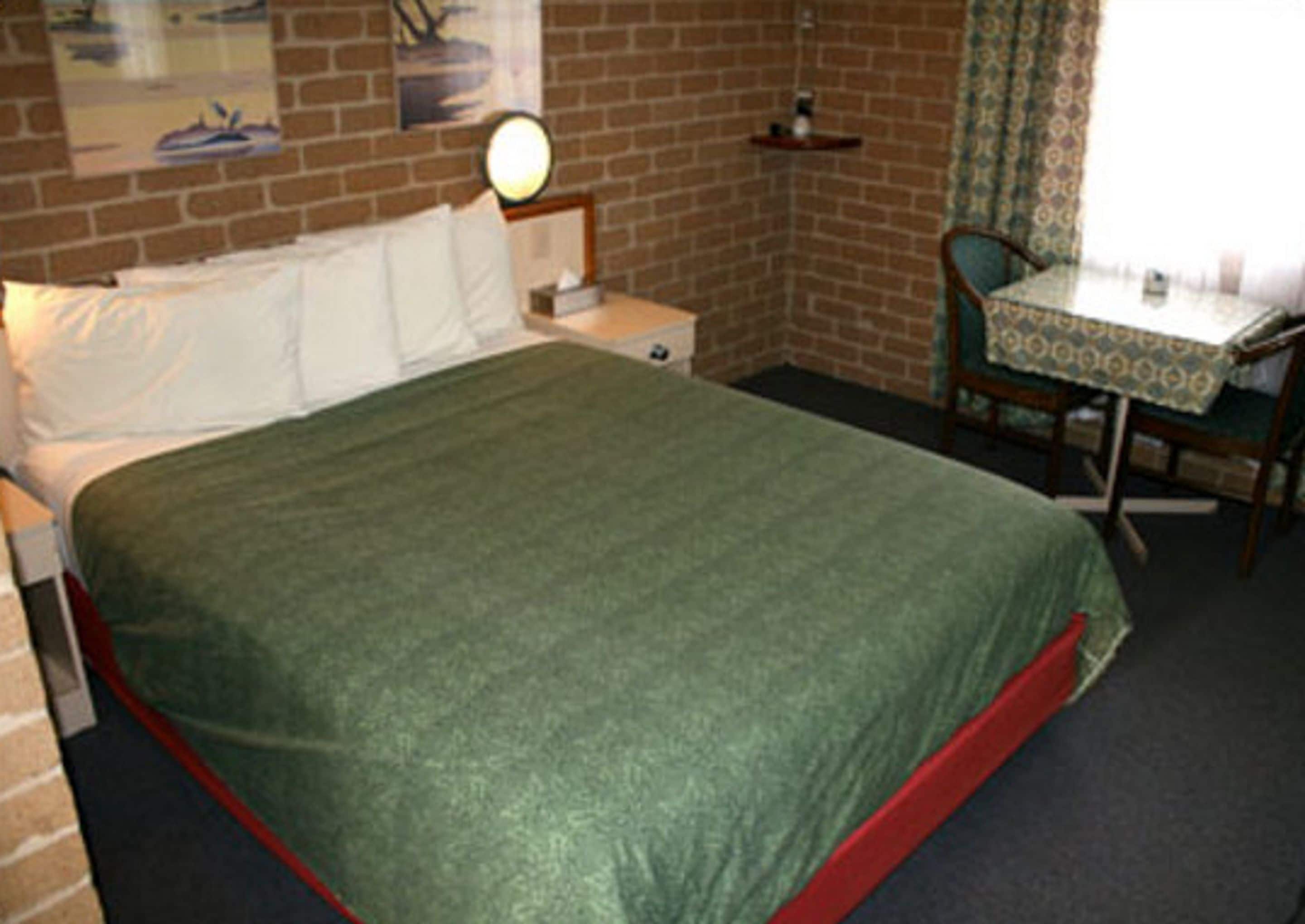 Een kamer met een bed, een stoel, een klein tafeltje en een wandklok.