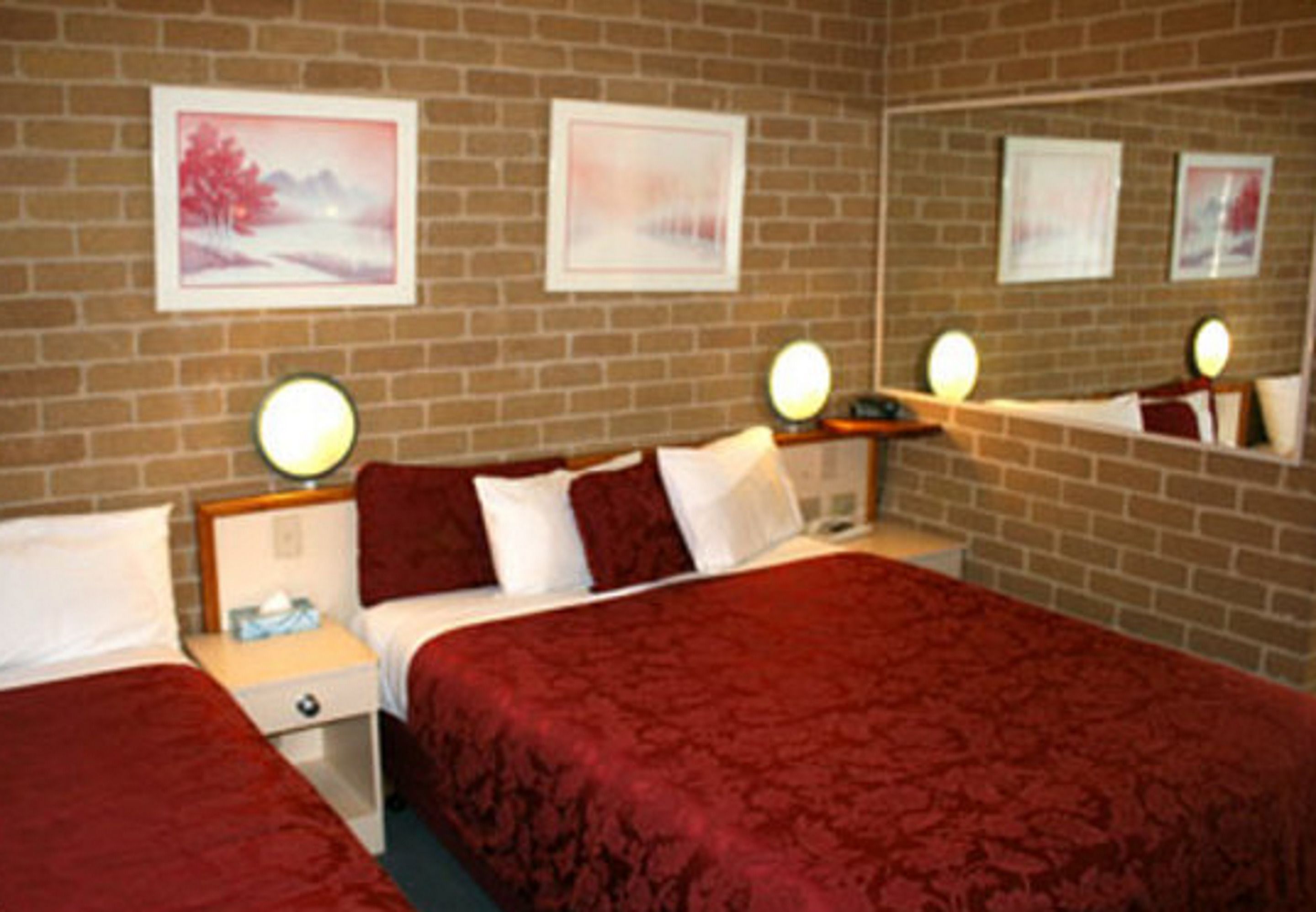 A hotel room with two beds, a brick wall, and framed pictures.